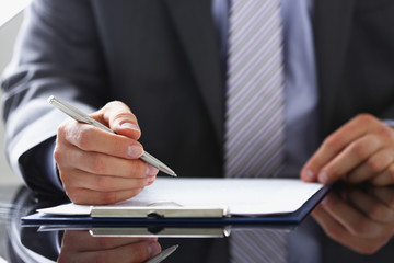 Male arm in suit and tie fill form clipped to pad with silver pen closeup. Sign gesture read pact...