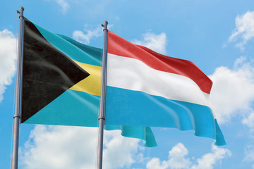 Luxembourg and Bahamas flags waving in the wind against white cloudy blue sky together. Diplomacy concept, international relations.