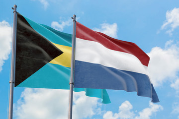 Netherlands and Bahamas flags waving in the wind against white cloudy blue sky together. Diplomacy concept, international relations.
