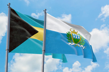 San Marino and Bahamas flags waving in the wind against white cloudy blue sky together. Diplomacy concept, international relations.