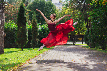 Woman ballerina in red ballet dress dancing in pointe shoes in autumn park.