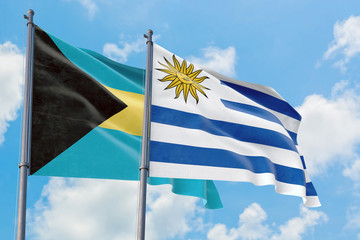 Uruguay and Bahamas flags waving in the wind against white cloudy blue sky together. Diplomacy concept, international relations.