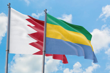 Gabon and Bahrain flags waving in the wind against white cloudy blue sky together. Diplomacy concept, international relations.