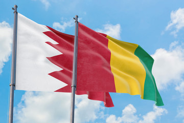 Guinea and Bahrain flags waving in the wind against white cloudy blue sky together. Diplomacy concept, international relations.