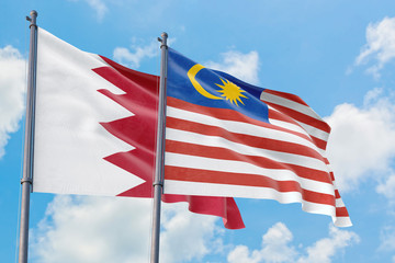 Malaysia and Bahrain flags waving in the wind against white cloudy blue sky together. Diplomacy concept, international relations.