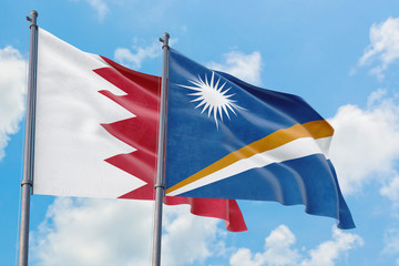 Marshall Islands and Bahrain flags waving in the wind against white cloudy blue sky together. Diplomacy concept, international relations.
