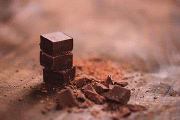 Chopped dark chocolate with cocoa on wooden table, selected focus, close up photo.