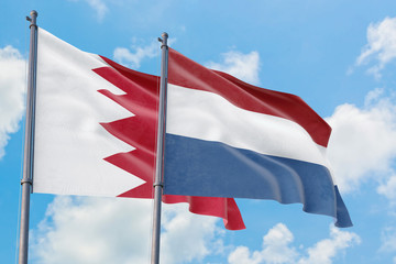 Netherlands and Bahrain flags waving in the wind against white cloudy blue sky together. Diplomacy concept, international relations.