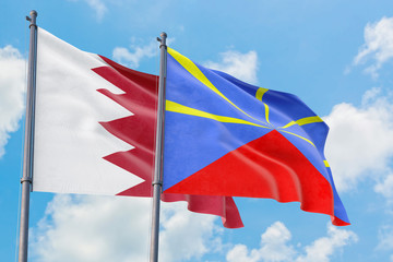 Reunion and Bahrain flags waving in the wind against white cloudy blue sky together. Diplomacy concept, international relations.