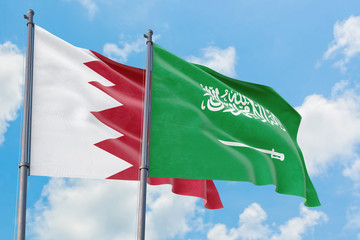 Saudi Arabia and Bahrain flags waving in the wind against white cloudy blue sky together. Diplomacy concept, international relations.