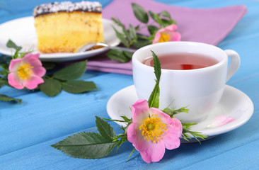 Cup of tea with cheesecake and wild rose flower on blue boards