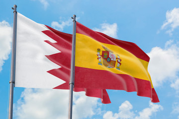 Spain and Bahrain flags waving in the wind against white cloudy blue sky together. Diplomacy concept, international relations.