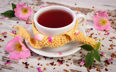 Cup of tea with wild rose flower on old rustic wooden background