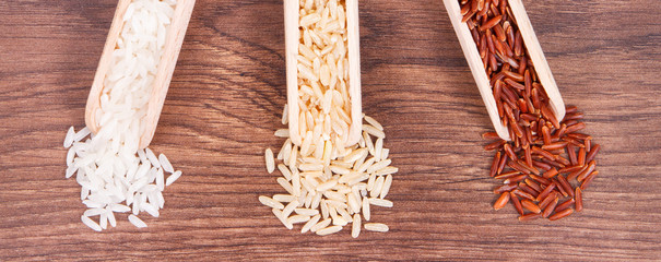 Fototapeta premium Red, brown and white rice with wooden scoop on rustic board, healthy food