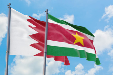 Suriname and Bahrain flags waving in the wind against white cloudy blue sky together. Diplomacy concept, international relations.