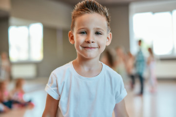 Portrait of a cute and happy little boy in white t-shirt looking at camera with smile while standing in the dance studio