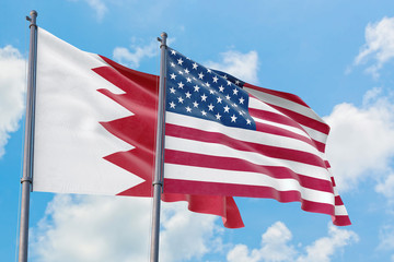 United States and Bahrain flags waving in the wind against white cloudy blue sky together. Diplomacy concept, international relations.