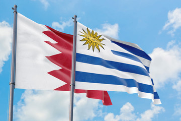 Uruguay and Bahrain flags waving in the wind against white cloudy blue sky together. Diplomacy concept, international relations.