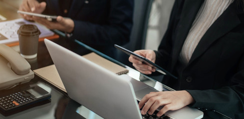 Business documents on office table with smart phone, tablet and laptop computer and graph with social network diagram and two colleagues discussing data in office.