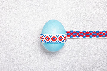 Blue shine egg with a national traditional ribbon on a silver glitter background