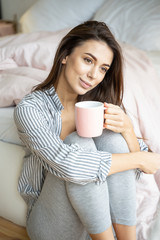 Dreamy young woman sitting by the bed