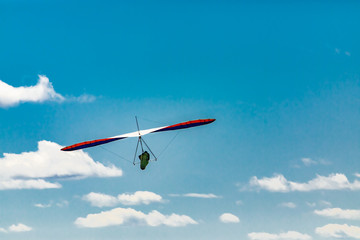 The extremal hobby of a brave person. Soaring hang gliding flight through the puffy clouds in the sky. View from the bottom