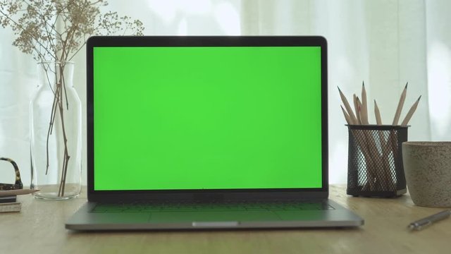 A computer laptop with green screen on the wooden table in home office