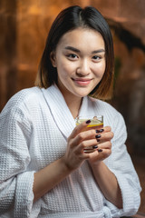 Beautiful Asian lady drinking tea after beauty procedures in salon