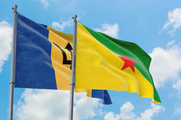 French Guiana and Barbados flags waving in the wind against white cloudy blue sky together. Diplomacy concept, international relations.