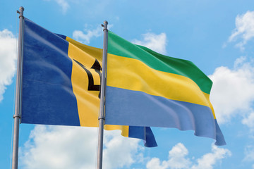 Gabon and Barbados flags waving in the wind against white cloudy blue sky together. Diplomacy...