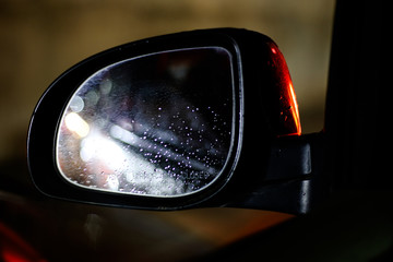 Car side-mirror with raindrops and reflection at night while driving
