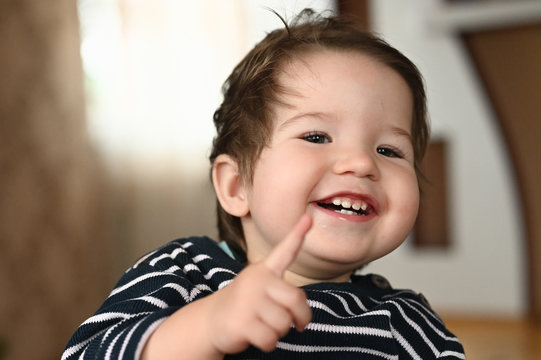 The Child Laughs And Shows A Finger. The Child Is 0-1 Years Old. A Small Child Shows A Finger With One Hand. One Year Old Child Portrait.