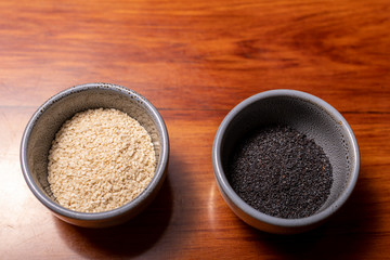 Slate-grey bowls of sesame and puppy seeds resting on a wooden bench