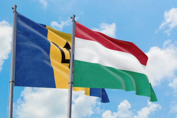 Hungary and Barbados flags waving in the wind against white cloudy blue sky together. Diplomacy concept, international relations.