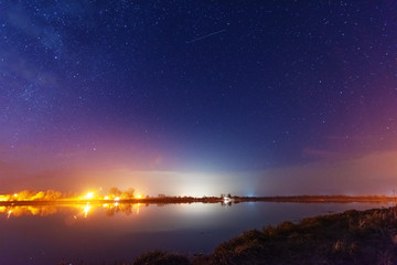 A magical starry night on the river bank with a large tree and a milky way in the sky and falling stars