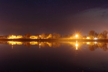 A magical starry night on the river bank with a large tree and a milky way in the sky and falling stars