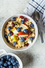 Bircher muesli or overnight oatmeal with apple, banana and blueberries in gray bowl, top view.
