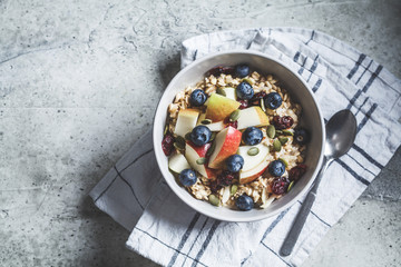 Bircher muesli or overnight oatmeal with apple, banana and blueberries in gray bowl, top view.