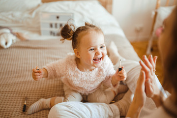 Little girl doing makeup to mom. Mother and daughter have fun together. The daughter paints lips to my mother. Happy loving family.