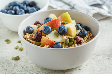 Bircher muesli or overnight oatmeal with apple, banana and blueberries in gray bowl.