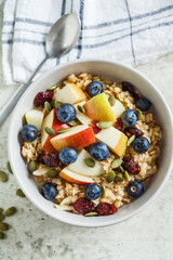 Bircher muesli or overnight oatmeal with apple, banana and blueberries in gray bowl, top view.