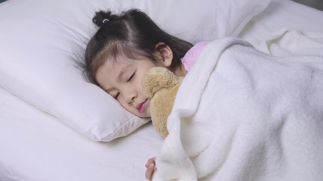Happy child little asian girl sleeping with her teddy bear on the bed in her bedroom, Educational concept for homeschool