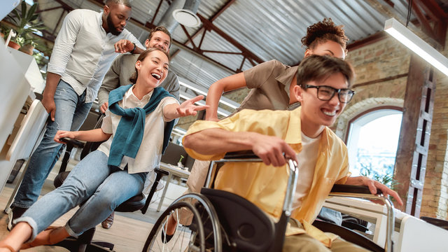 Staying positive. Young happy asian man in wheelchair having fun with his colleagues at modern office