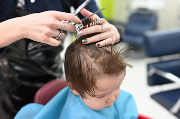 A child at the hairdresser. The first haircut of the child at the hairdresser. Baby haircut toddler.