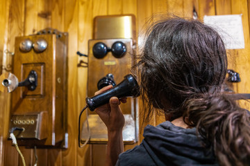 A young man calling via 1900s wood wall telephone. Man making a call to the past. Vintage phone in the museum,Kootenays, British Columbia, Canada