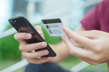 Close-up human hands with mobile phone and credit card. Person holds smartphone and bank card, closeup shot. On foreground male hands hold cell phone and card. Soft focus effect. Outdoors. In the city