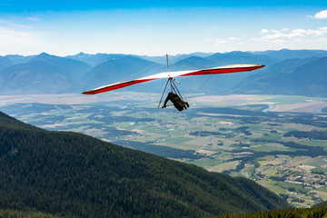 Fototapeta na wymiar Long shot of flying extremal hang glider. Young man enjoying his recreational journey to Creston, British Columbia, Canada