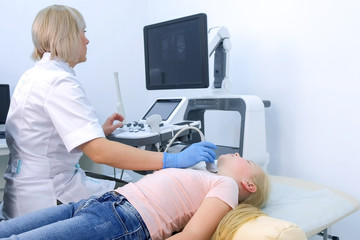 Woman doctor examining patient's child girl thyroid gland using ultrasound scanner machine. Woman runs ultrasound sensor over patient's neck and looking at screen. Diagnostic examination.