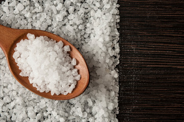 Fototapeta na wymiar Sea salt in wooden spoon on the kitchen table. top view