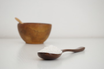 Wooden spoon and bowl with salt on the white table